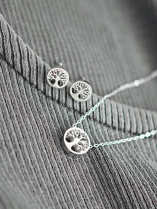 Silver tree of life earrings and necklace on a textured surface