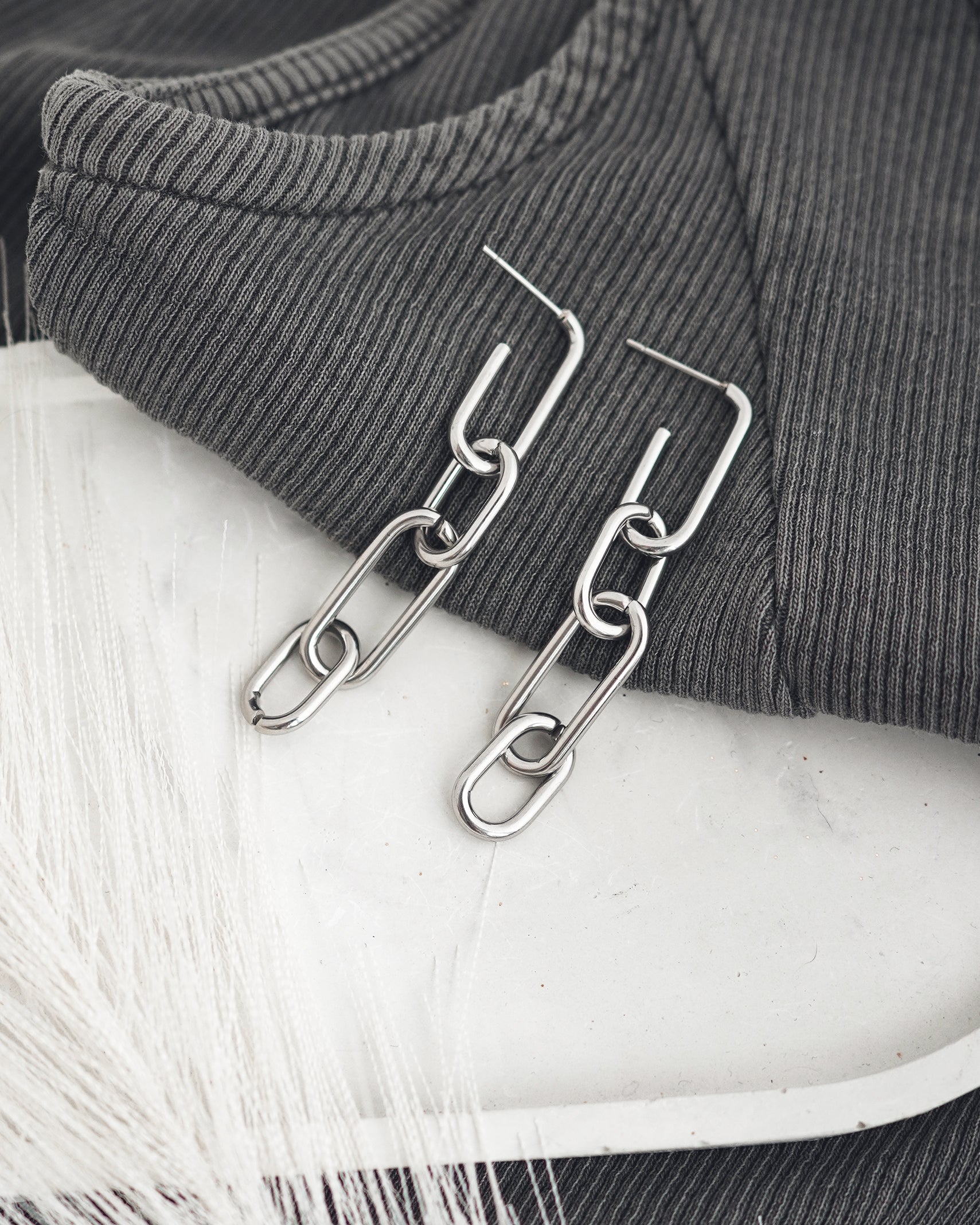 Silver colored chain earrings accessories on a white plate with gray t-shirt.