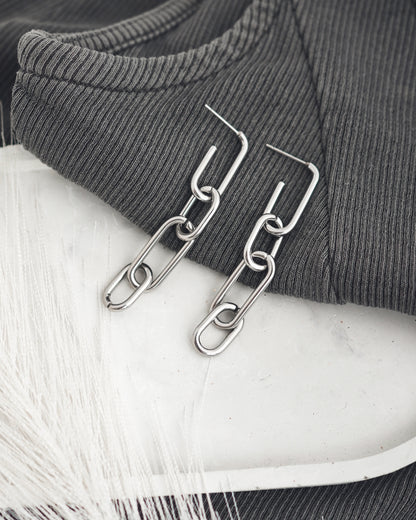 Silver colored chain earrings accessories on a white plate with gray t-shirt.