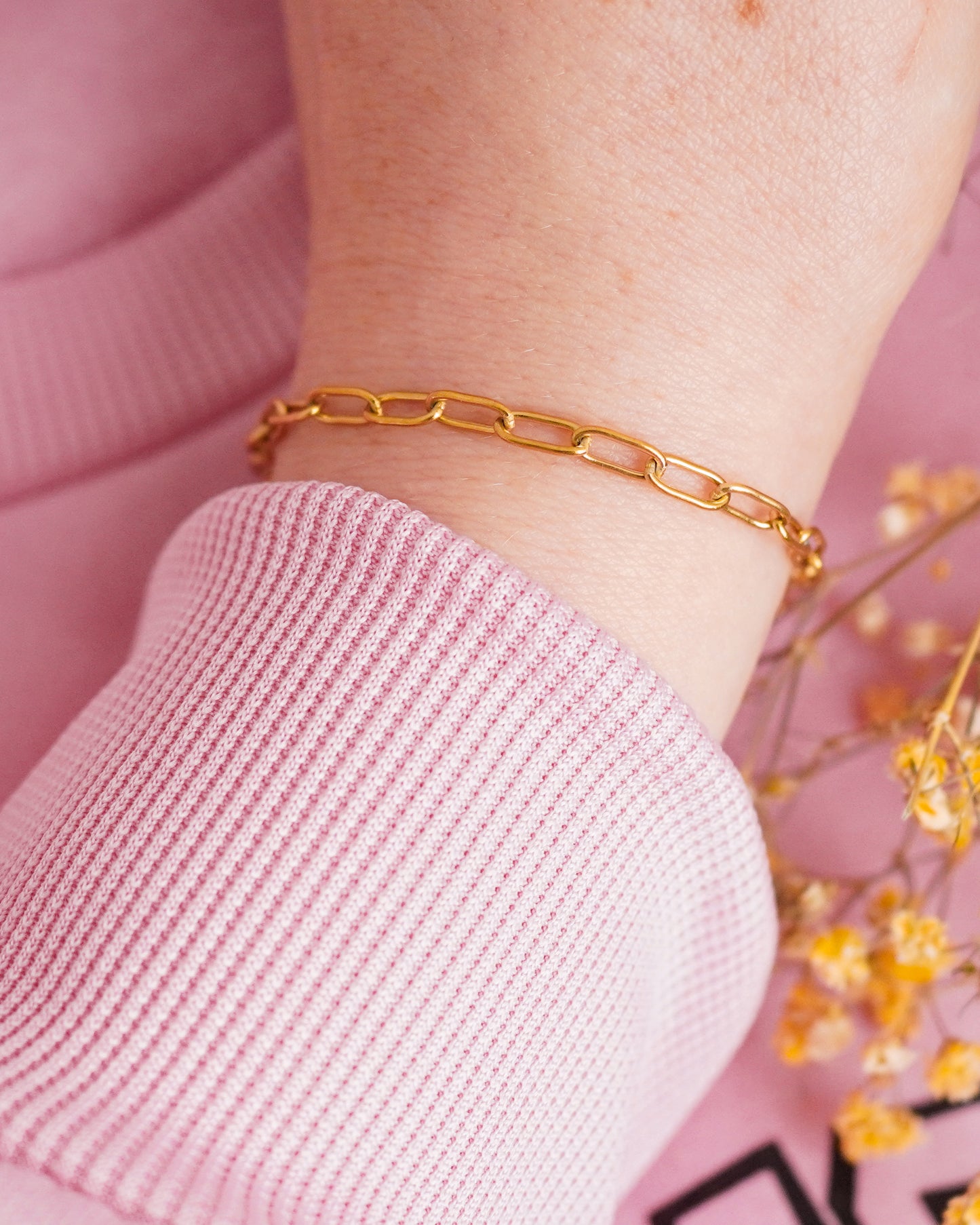 Gold chain bracelet on a wrist with a pink sleeve and blurred background