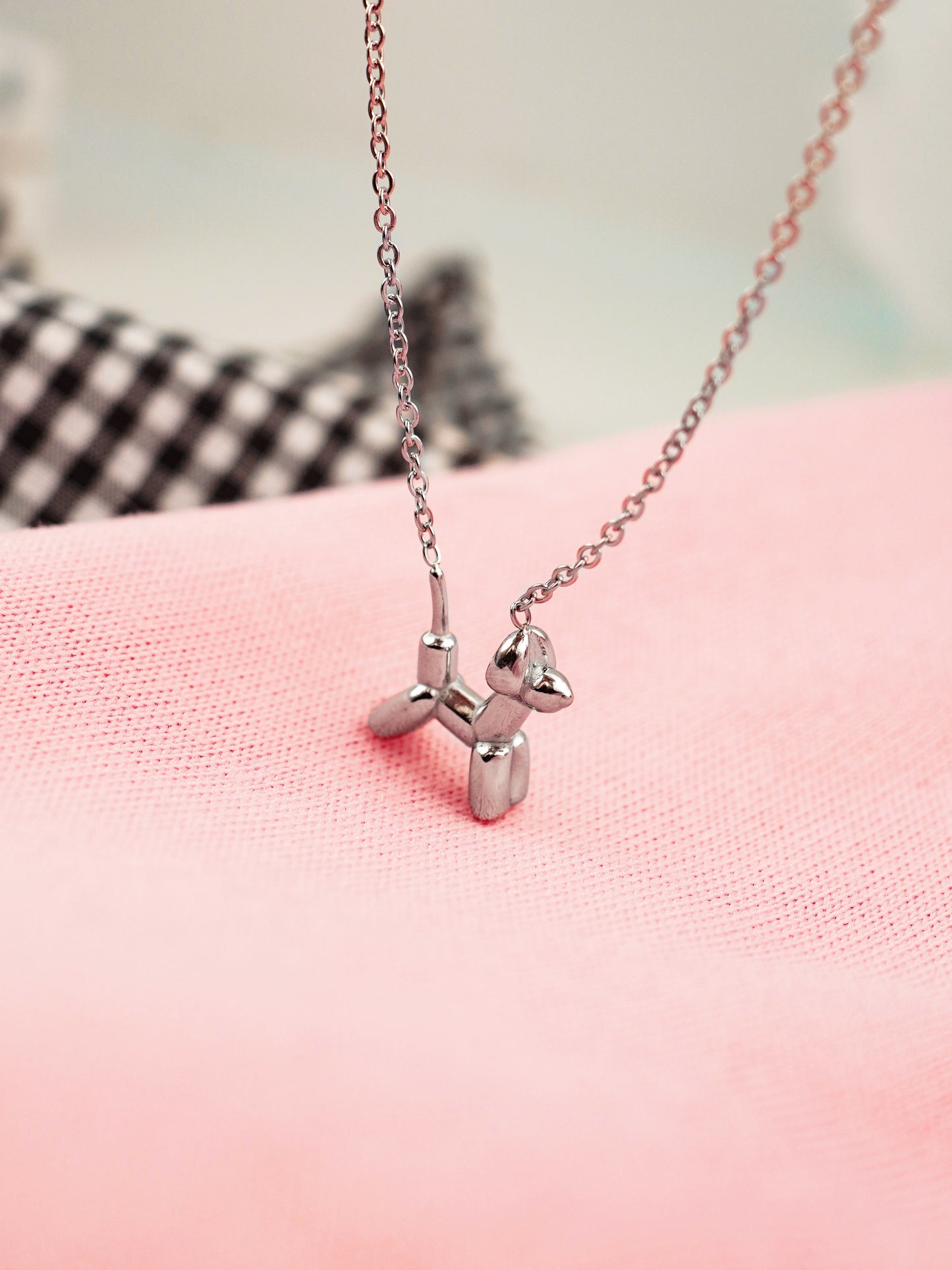 Silver balloon dog necklace on a pink surface with a blurred background