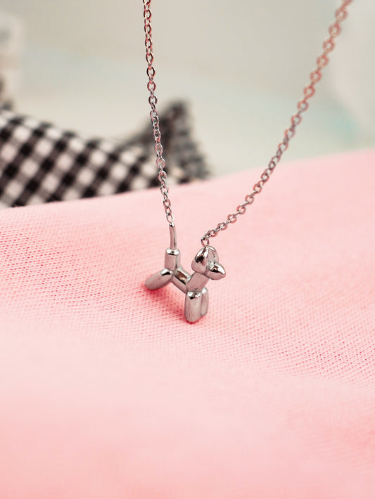 Silver balloon dog necklace on a pink surface with a blurred background