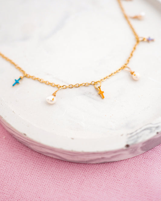 Gold necklace with small pendants on a white dish with a pink background