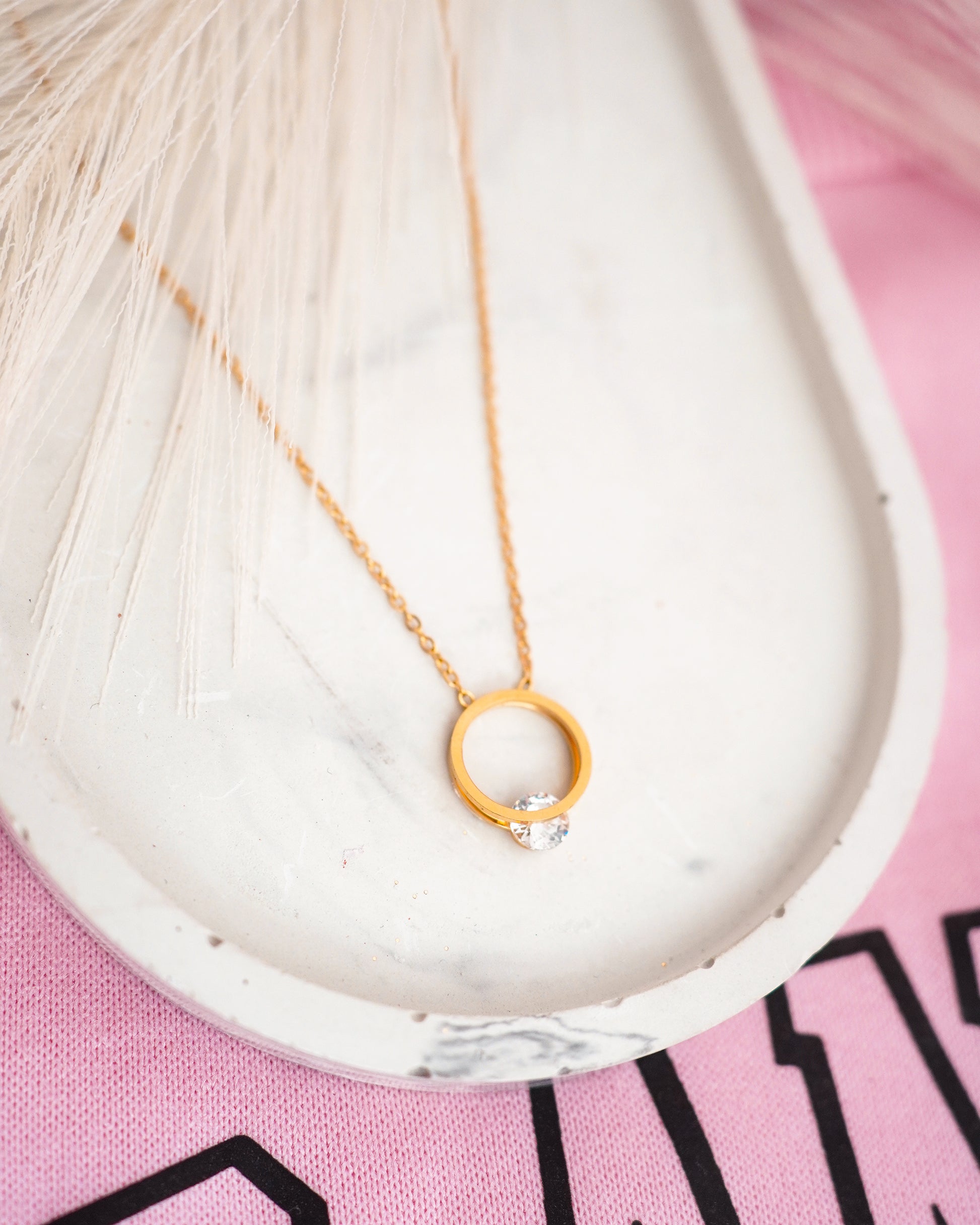 Gold-plated necklace with a circular pendant on a pink surface