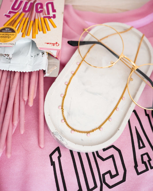Gold-plated necklace on a white stand with pink background and product packaging.