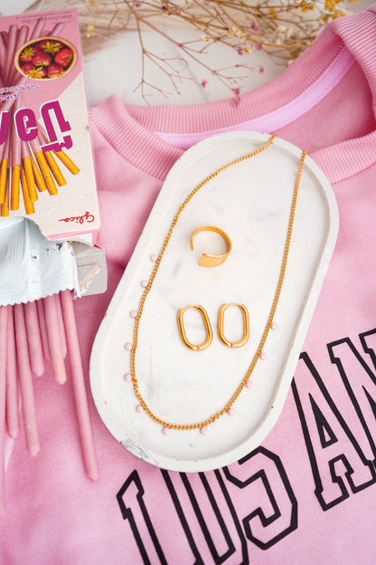 Gold-plated ring, necklace and earrings on a pink sweatshirt with visible text