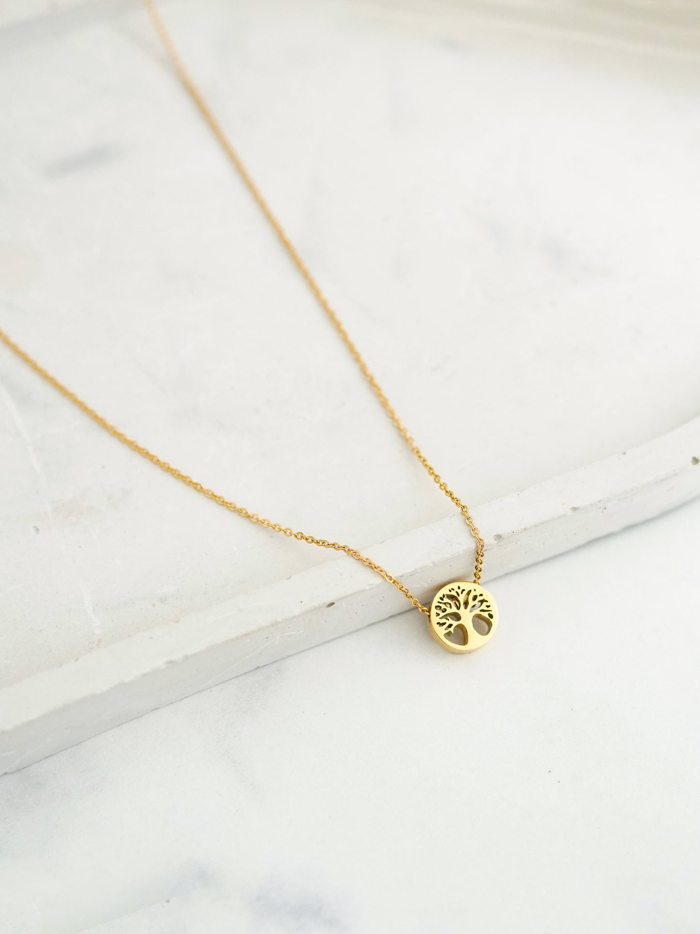 Gold necklace with a tree of life pendant on a marble surface