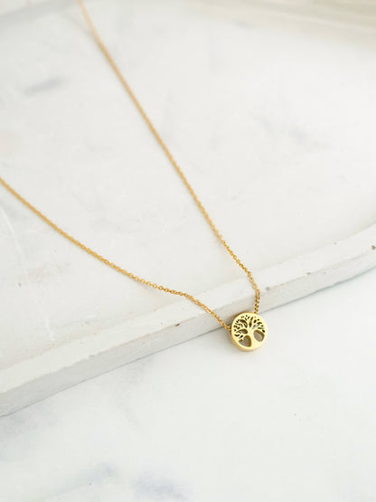 Gold necklace with a tree of life pendant on a marble surface