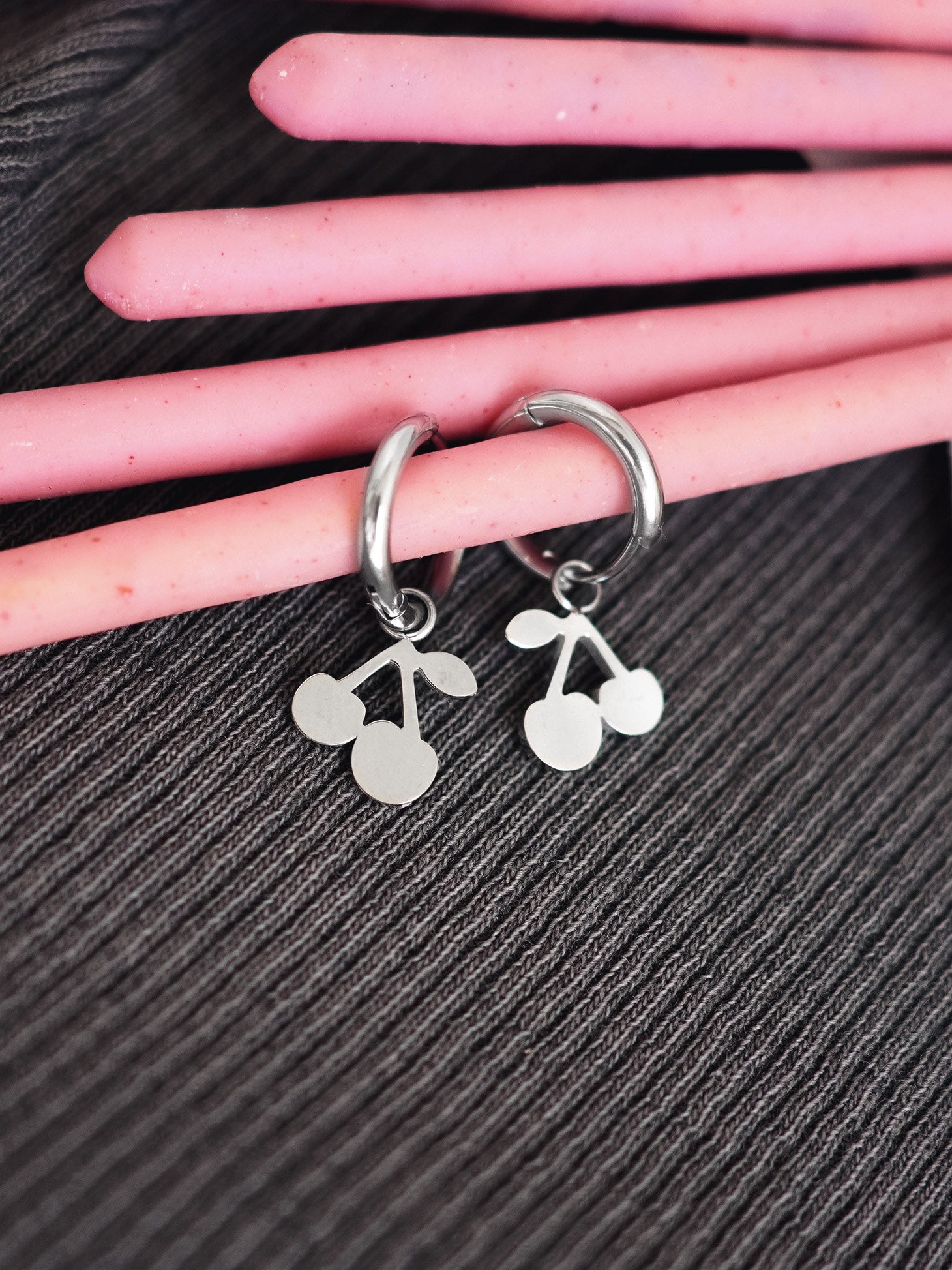 Silver hoop earrings with cherry designs on a hand against a black background