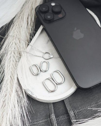 Silver earrings on a white surface with a black phone and gray fabric background