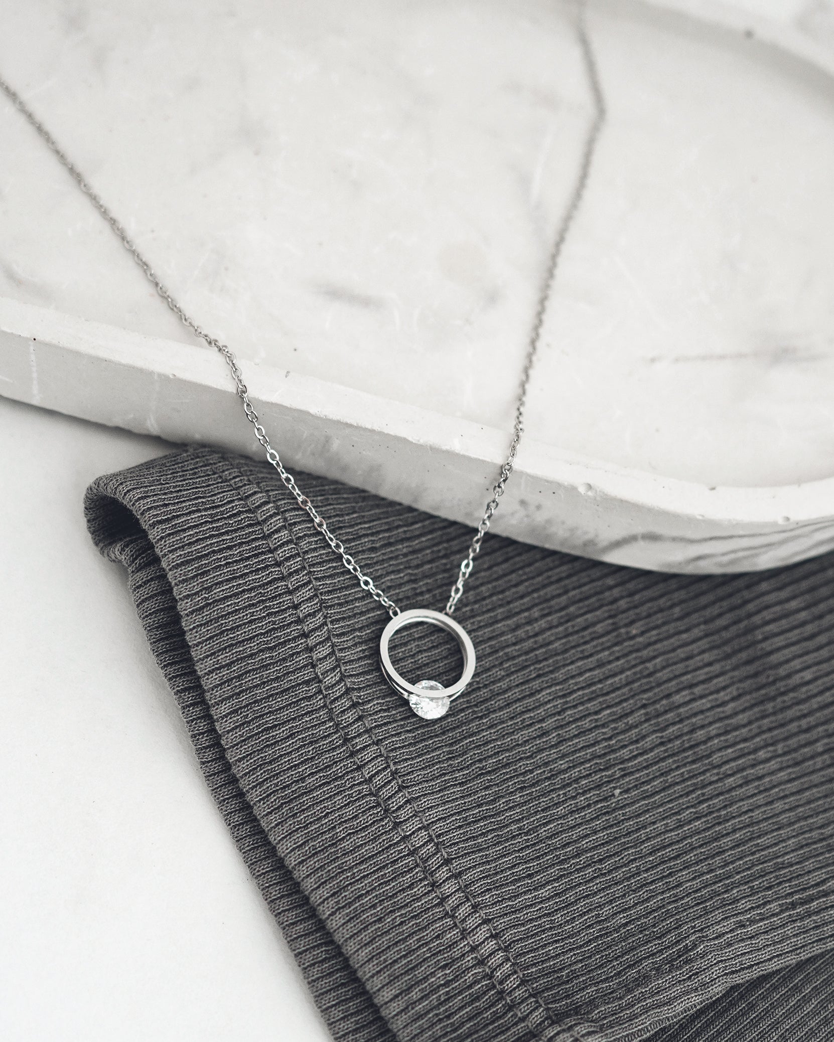 Silver necklace with a small pendant on a textured surface