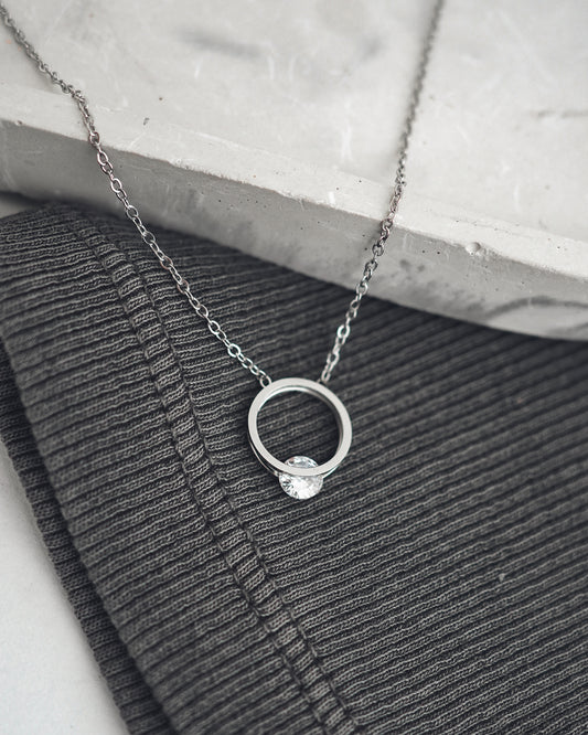 Silver necklace with a ring pendant on a textured surface