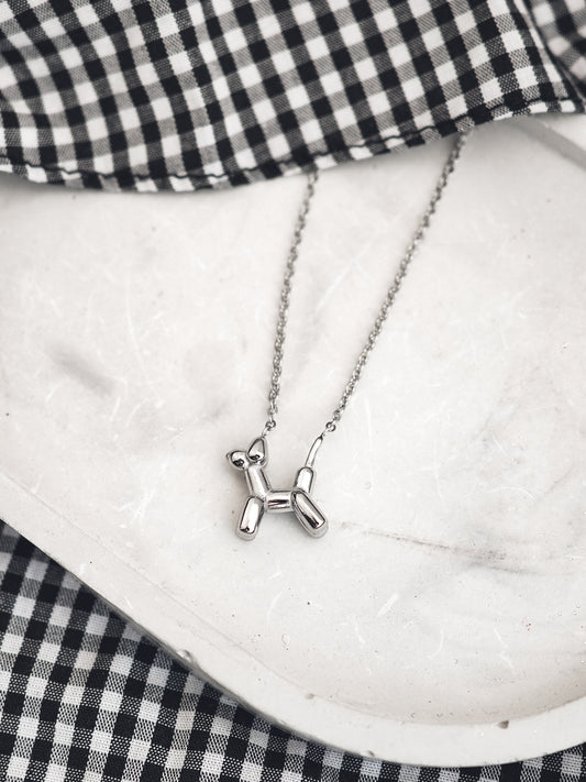 Silver balloon dog necklace on a white surface with a black and white checkered fabric background