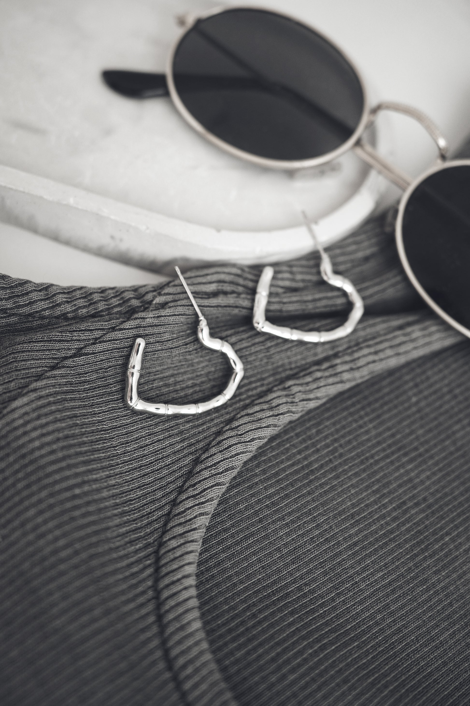 Heart-shaped earrings on a textured surface with sunglasses in the background
