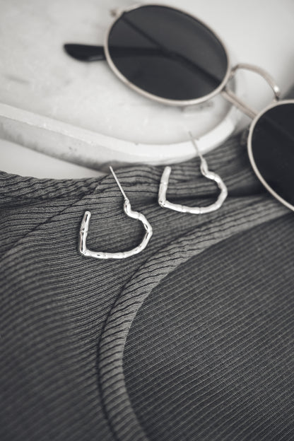 Heart-shaped earrings on a textured surface with sunglasses in the background
