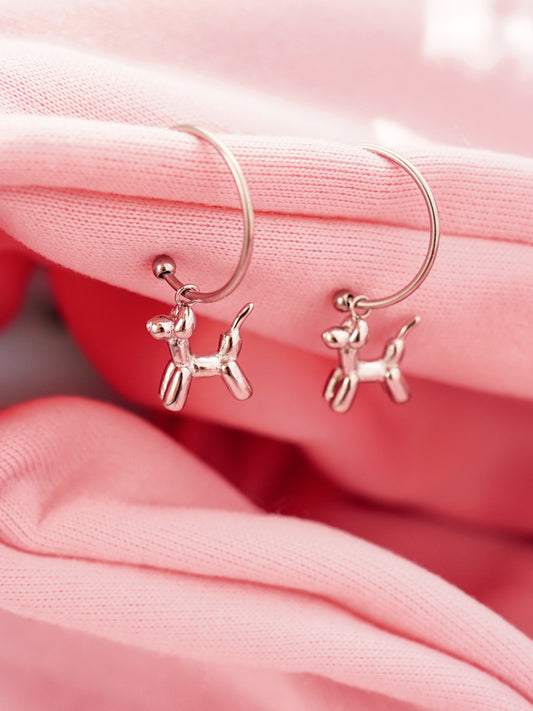 Silver stud earrings with dog-shaped charms on a pink fabric background