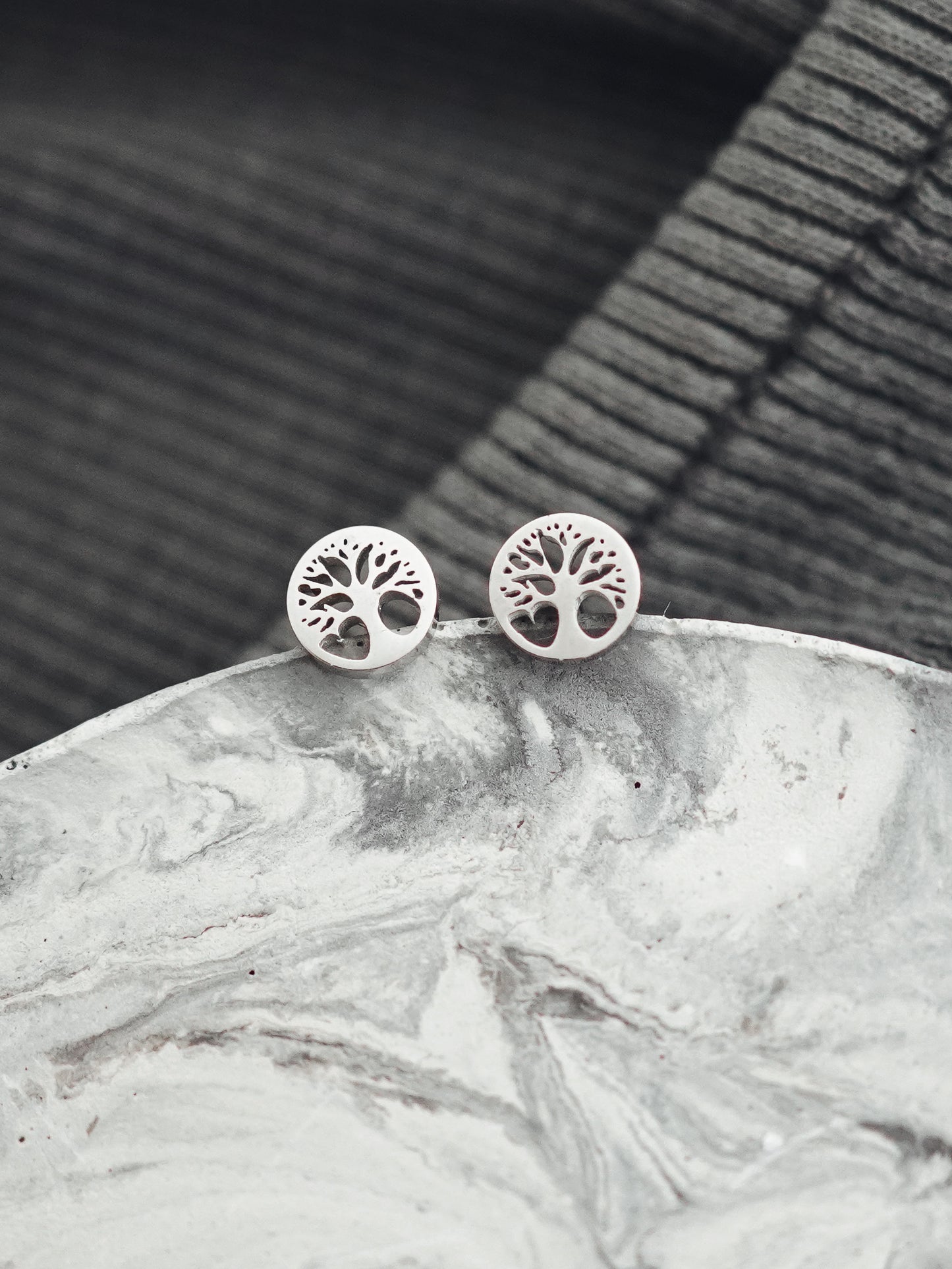 Silver tree-of-life earrings on a marble surface with a dark woven background