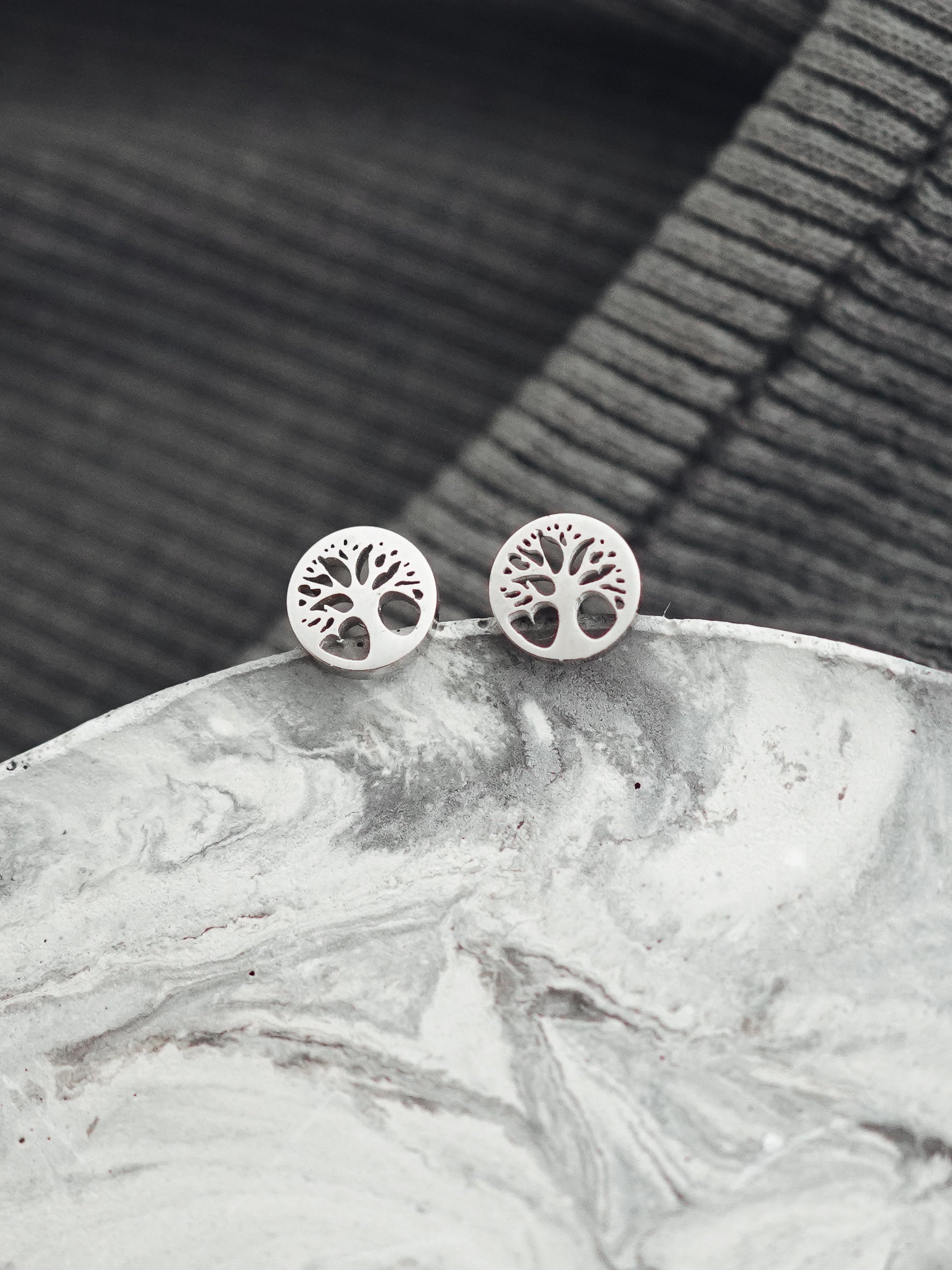 Silver tree-of-life earrings on a marble surface with a dark woven background