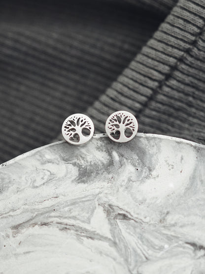 Silver tree-of-life earrings on a marble surface with a dark woven background