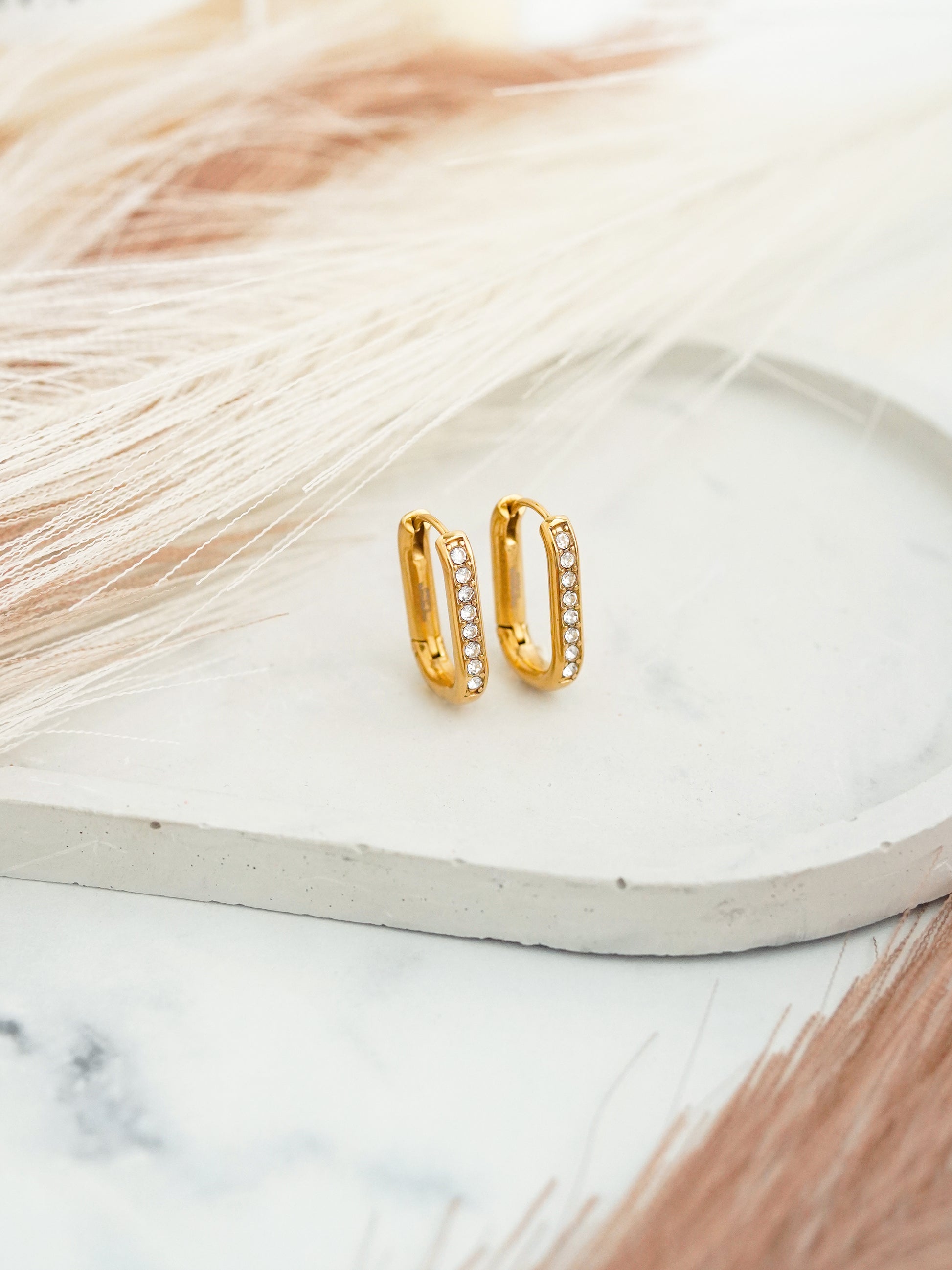 Gold-plated stainless steel hoop earrings with embedded crystals on a marble surface