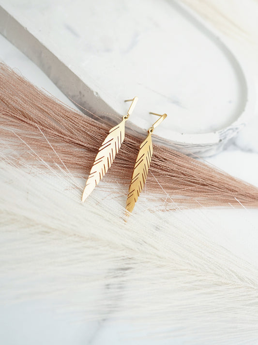 Gold-plated  feather-shaped earrings on a marble surface with feathers.