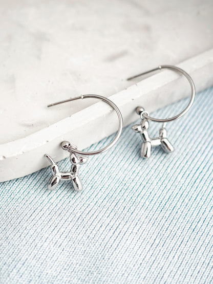 Silver stud earrings with balloon dog charms on a light blue fabric background