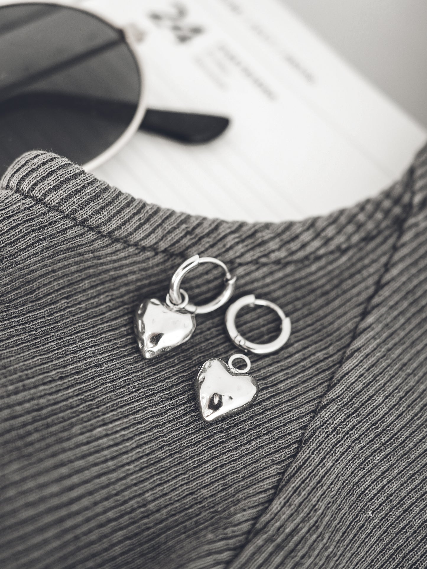 Silver heart-shaped earrings on a textured fabric background